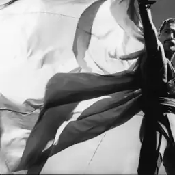 Freddie Mercury on stage with one arm raised, holding a large pale cape